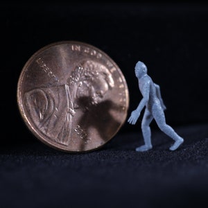 May include: A small, gray figurine of a person running away from a 2006 US penny. The penny is facing the viewer with the head of Abraham Lincoln visible.