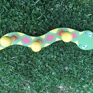 May include: A green snake-shaped wooden coat rack with yellow knobs and red and yellow diamond patterns.