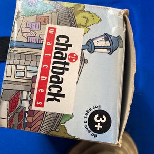 May include: A cardboard box for Chatback watches, featuring a street scene illustration with a lamppost. The box has the text "Chatback watches" in red and white. It also has a "3+" age recommendation.