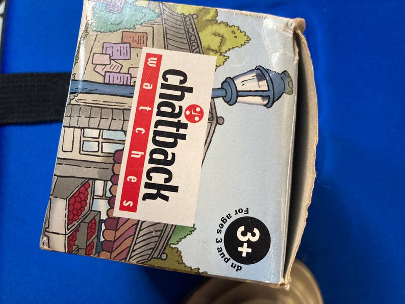 May include: A cardboard box for Chatback watches, featuring a street scene illustration with a lamppost. The box has the text "Chatback watches" in red and white. It also has a "3+" age recommendation.