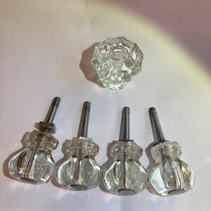 May include: Five clear glass cabinet knobs with silver metal screws. The knobs have a faceted design and are round with a slight indentation in the center.