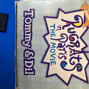 May include: A light blue box featuring the text "Tommy & Dil" in blue and "Rugrats in Paris: The Movie" in a starburst design. The Nickelodeon logo is visible in orange.