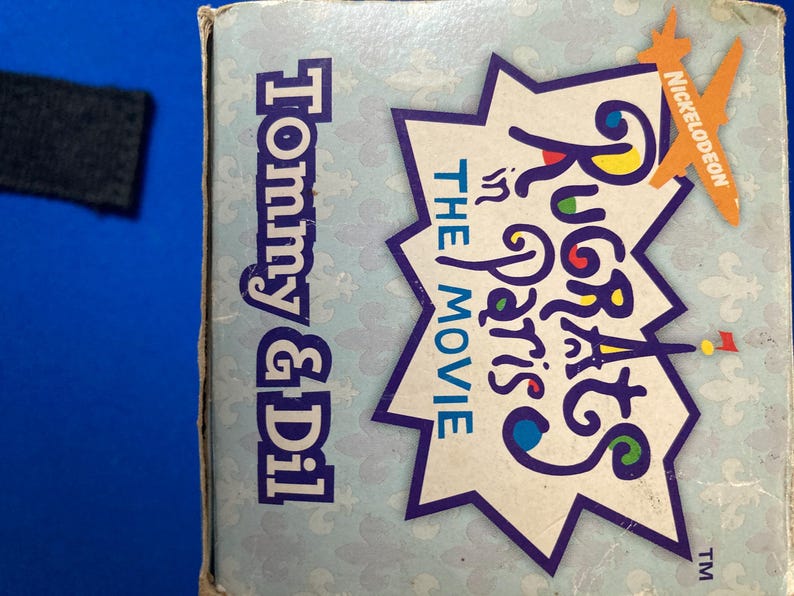 May include: A light blue box featuring the text "Tommy & Dil" in blue and "Rugrats in Paris: The Movie" in a starburst design. The Nickelodeon logo is visible in orange.