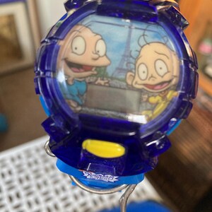 May include: A blue digital watch featuring cartoon characters with the Eiffel Tower in the background. The watch has a blue strap and yellow accents. The watch face displays two cartoon characters.