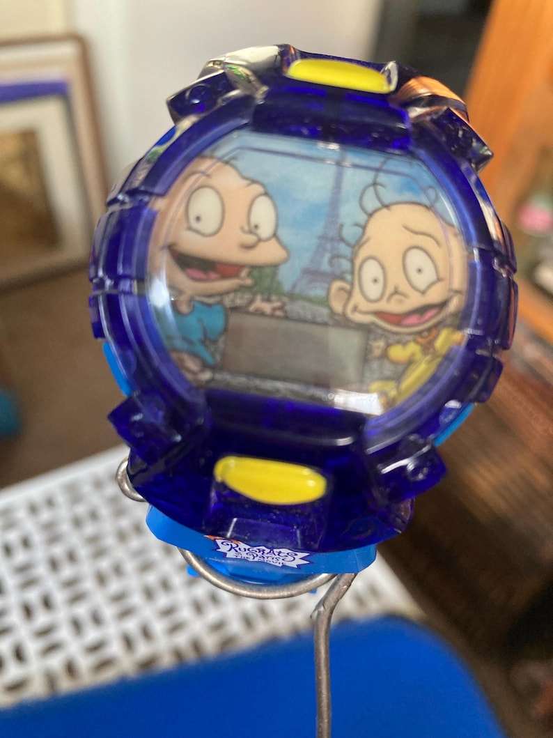May include: A blue digital watch featuring cartoon characters with the Eiffel Tower in the background. The watch has a blue strap and yellow accents. The watch face displays two cartoon characters.