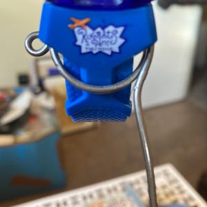 May include: A blue bottle stopper with a silver metal handle. The stopper has the text "Rugrats" in white script inside a starburst design. The top of the stopper is a dark blue, possibly glass.