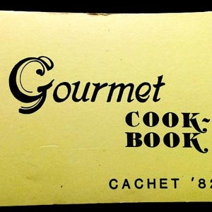 May include: A yellow cookbook with a black and white title that reads "Gourmet Cookbook" and "Cachet '82-'83".