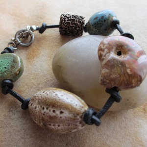 May include: A leather bracelet with a variety of colorful ceramic and stone beads. The beads include green, blue, brown, and white.