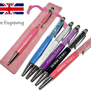 May include: A collection of colorful pens with crystal-filled barrels and touch screen tips. Each pen is engraved with a name and the text "TEAM C". A pink pen case and the text "Free Engraving" are also visible.
