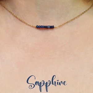 Könnte beinhalten: Eine zarte goldene Kettenkette mit einer Leiste aus kleinen, dunkelblauen Saphirperlen. Die Kette liegt auf dem Hals eines Models und das Wort "Saphir" ist in blauer Schrift unterhalb der Kette geschrieben.