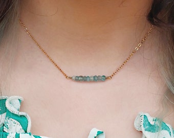 May include: A gold chain necklace with a delicate bar of light blue gemstones.