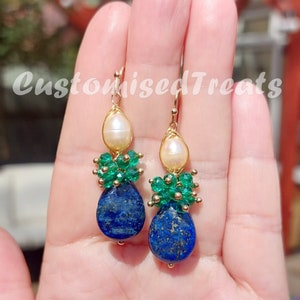 Könnte beinhalten: Goldene Ohrringe mit einem tropfenförmigen Lapislazuli-Stein, einer Perle und grünen Smaragdperlen.