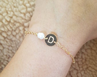 May include: A gold chain bracelet with a single pearl charm and a round charm with the letter "D" engraved on it.