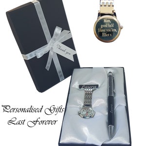 May include: A black gift box with a white ribbon and a silver watch and pen set in a black box with white lining. The watch has a silver band and a white face. The pen is black with silver accents. The watch and pen are both engraved with the name "Laura". The watch also has a message engraved on the back that reads "Mam, good luck! I love you lots, Elliot x".