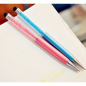 May include: Two pens with a stylus tip, one pink and one blue, are displayed on a white surface. The upper barrel of each pen is filled with sparkling crystals. The pens have silver-colored metal accents.
