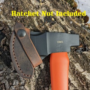 May include: A brown leather sheath with a snap closure for a small hatchet. The sheath is attached to a black and orange hatchet with a black handle and the text "CRKT" on the head.