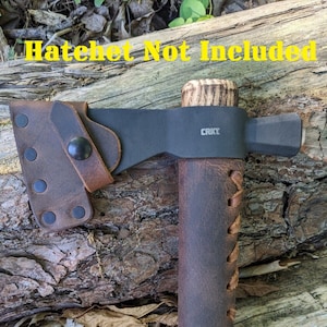 May include: A brown leather sheath with a black handle and a black head. The head has the text "CRKT" on it. The text "Hatchet Not Included" is written in yellow on a wooden surface behind the sheath.