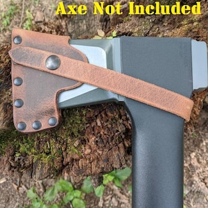 May include: A brown leather axe sheath with a strap and rivets, designed to fit an axe. The sheath is shown on an axe with a black handle and a gray head. The text "Axe Not Included" is visible in yellow.