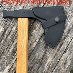May include: A black hatchet head with a wooden handle, featuring a leather sheath secured by a snap. The hatchet head has a hammer on one side and a small emblem on the other. The text "Hatchet Not Included" is visible.