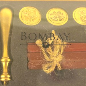 May include: A gold-colored wax seal stamp set with the word "BOMBAY" printed on the box. The set includes a gold stamp, wax sticks, and gold-colored wax seals with various designs.