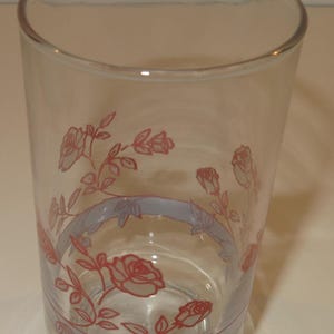 May include: A clear glass drinking glass with a blue and white band around the middle and a pink rose pattern.