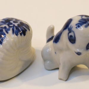 Puede incluir: Dos pequeñas figuritas de porcelana, una de un perro y otra de un caracol, ambas pintadas con un patrón floral azul y blanco.