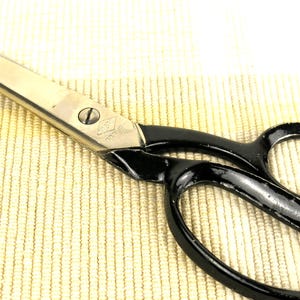 Könnte beinhalten: Ein Paar großer Scheren mit silbernen Klingen und schwarzen Griffen. Die Schere hat ein klassisches Design mit einer Schraube am Drehpunkt. Die Griffe haben Fingerlöcher für einen einfachen Griff. Die Schere ist wahrscheinlich zum Schneiden von Stoff oder Papier.