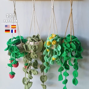 May include: Four handmade crochet hanging planters with various green and yellow plant designs. The planters are suspended from a wooden rack by white and tan cords. One planter features red strawberry accents. The image includes the text "PDF PATTERN" and flags.
