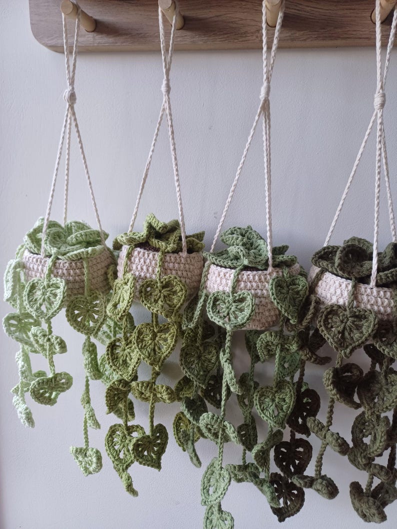 May include: Four crocheted hanging planters with green leaves. The planters are made of beige yarn and are hanging from a wooden shelf.