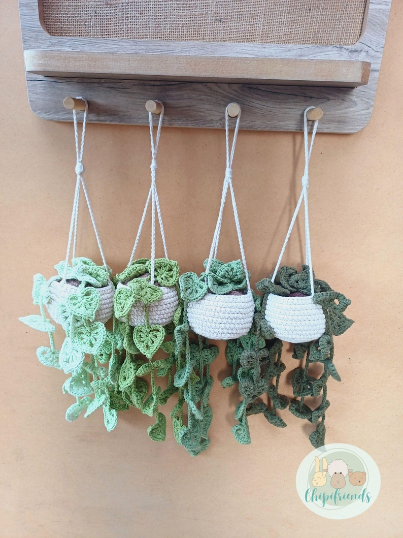 May include: Four crocheted hanging planters with green leaves, each in a white pot, hanging from hooks on a wooden wall.