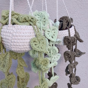 May include: Two crocheted hanging plant pots with green and brown crocheted leaves. The pots are white and have a rope hanger.