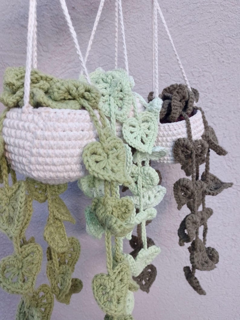 May include: Two crocheted hanging plant pots with green and brown crocheted leaves. The pots are white and have a rope hanger.
