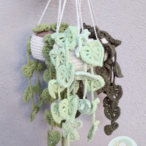 May include: Three crocheted hanging planters with green and brown leaves. The planters are made of white yarn and have a brown fabric lining. The planters are hanging from white yarn strings.