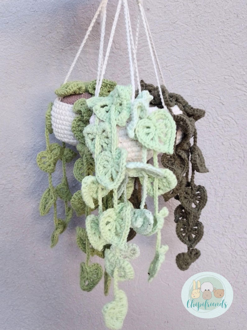 May include: Three crocheted hanging planters with green and brown leaves. The planters are made of white yarn and have a brown fabric lining. The planters are hanging from white yarn strings.