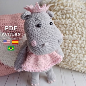 May include: Crochet pattern for a gray hippopotamus wearing a pink dress and a crown. The pattern is available in English, Spanish, and Portuguese. PDF pattern.