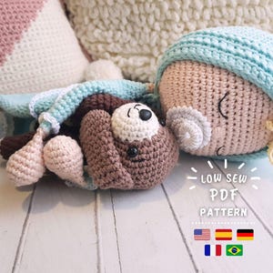 Puede incluir: Una mu&ntilde;eca de crochet con una manta azul y un osito de peluche de crochet marr&oacute;n. La mu&ntilde;eca est&aacute; durmiendo con los ojos cerrados. El texto "Low Sew PDF Pattern" est&aacute; impreso debajo de la mu&ntilde;eca. La imagen tambi&eacute;n incluye banderas de Estados Unidos, Espa&ntilde;a, Alemania, Francia y Brasil.
