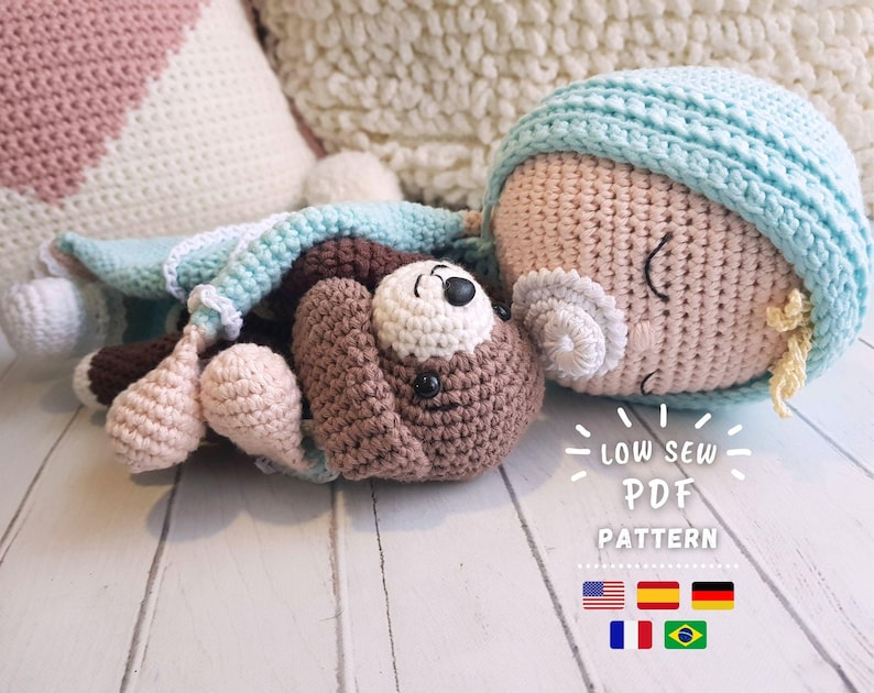 Puede incluir: Una mu&ntilde;eca de crochet con una manta azul y un osito de peluche de crochet marr&oacute;n. La mu&ntilde;eca est&aacute; durmiendo con los ojos cerrados. El texto "Low Sew PDF Pattern" est&aacute; impreso debajo de la mu&ntilde;eca. La imagen tambi&eacute;n incluye banderas de Estados Unidos, Espa&ntilde;a, Alemania, Francia y Brasil.
