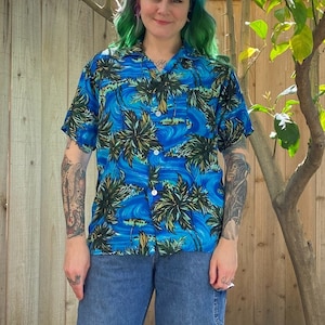 Mid century 1950’s blue men’s Hawaiian shirt with palm tree print. Rayon material. Buttons down the front with one pocket on the front.