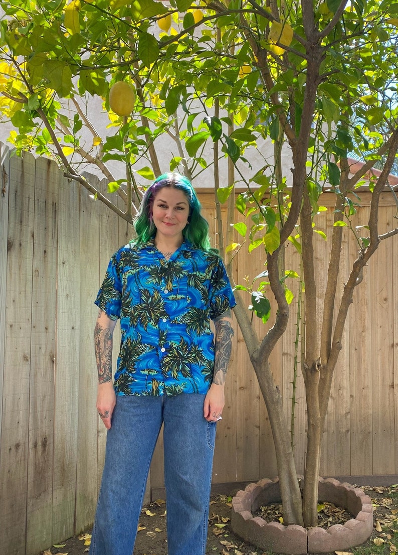 Mid century 1950’s blue men’s Hawaiian shirt with palm tree print. Rayon material. Buttons down the front with one pocket on the front.