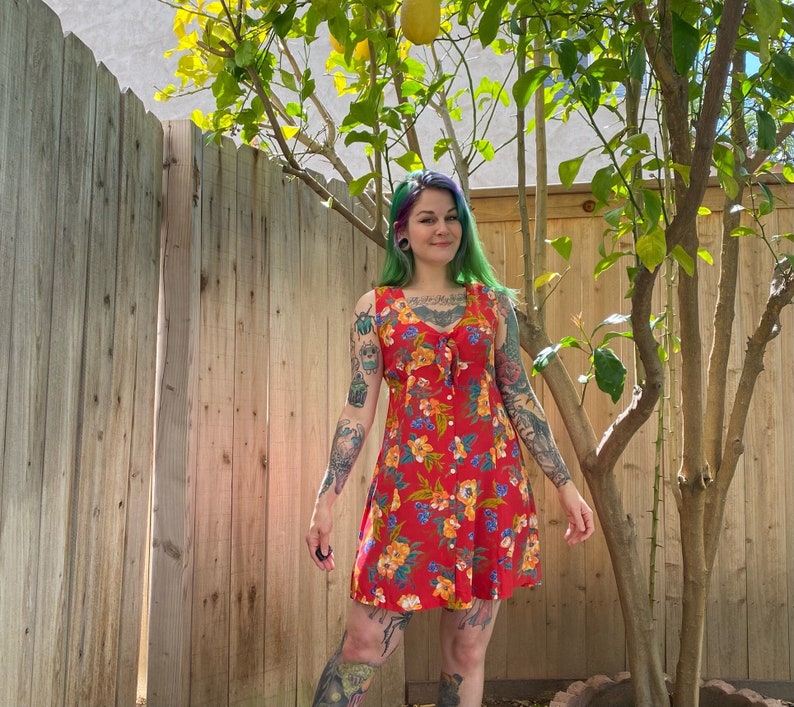 1990’s red and yellow floral Print mini dress by Gap. Red background with yellow and green floral print with blue raspberry print. Buttons down the front with a tie at the top. Size small