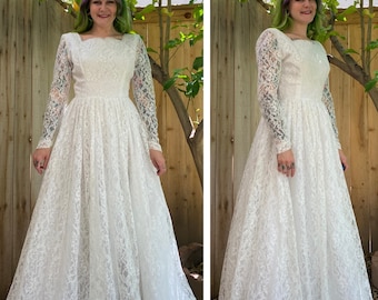 May include: A white lace wedding dress with long sleeves and a square neckline. The dress has a full skirt and is made of delicate lace.