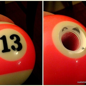 Pu&ograve; includere: Un pomello del cambio personalizzato a forma di palla da biliardo, con il numero 13 in nero su un cerchio bianco, su sfondo rosso. La seconda immagine mostra l'interno filettato.