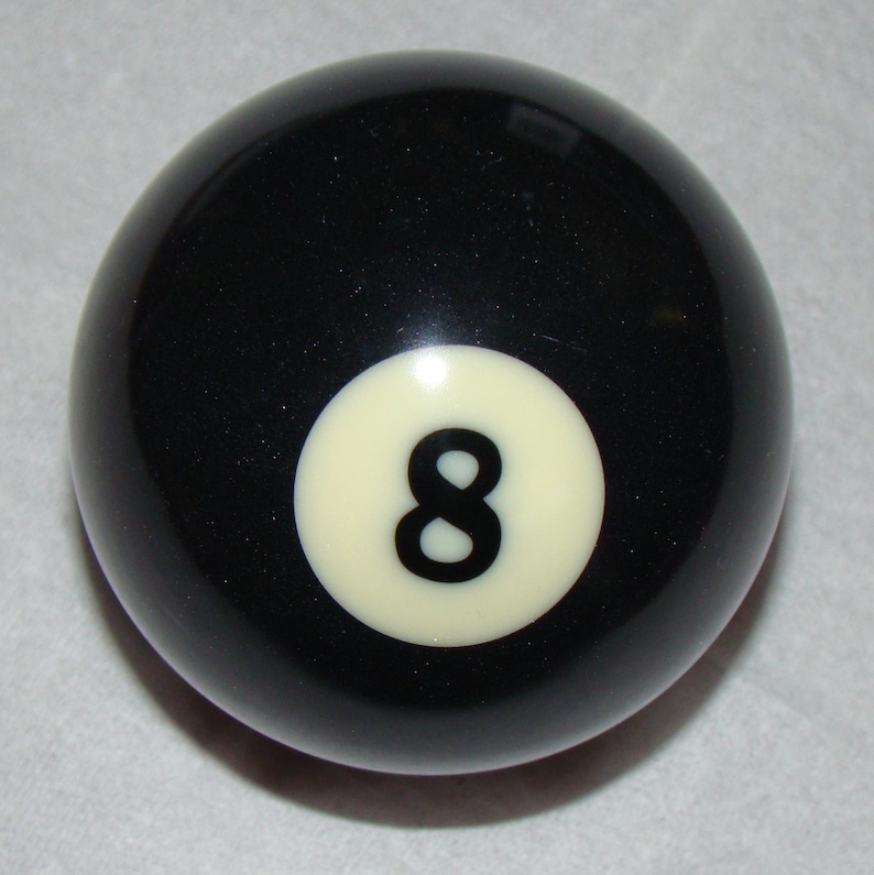 Pu&ograve; includere: Una palla da biliardo nera con un cerchio bianco con il numero 8 in nero. La palla ha una superficie liscia e lucida, utilizzata nel gioco del biliardo.
