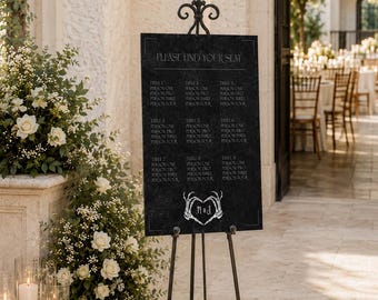 May include: A black rectangular wedding seating chart sign with white text reading PLEASE FIND YOUR SEAT and a skeletal hand heart graphic, displayed on a black metal easel with a decorative fleur-de-lis top and curved legs.