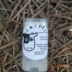 Puede incluir: Un stick de desodorante blanco con una ilustración de vaca en blanco y negro y el texto "ATPIZ" y "www.soapmuffin.com". El texto debajo de la ilustración dice "Tallow Deodorant", "sebo de pasto, cera de abejas, polvo de arrowroot, bicarbonato de sodio, aceite esencial".