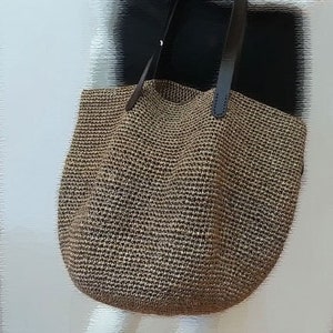 May include: A large, brown woven tote bag with black leather handles. The bag is made of a tightly woven material and has a slightly rounded shape.