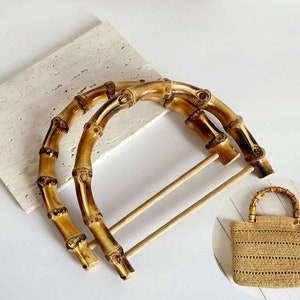 May include: Two brown bamboo handles for a bag. The handles are made of natural bamboo and have a rustic look. The handles are shown with a small straw bag with a bamboo handle.