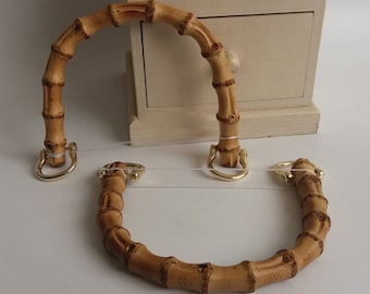 May include: Two brown bamboo handbag handles with gold metal hardware. The handles are curved and have a smooth, natural finish.