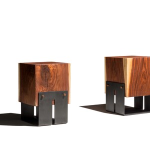 May include: Two wooden cube stools with a natural wood grain finish. Each stool has a dark metal base with a rectangular design. The stools are displayed on a white background.