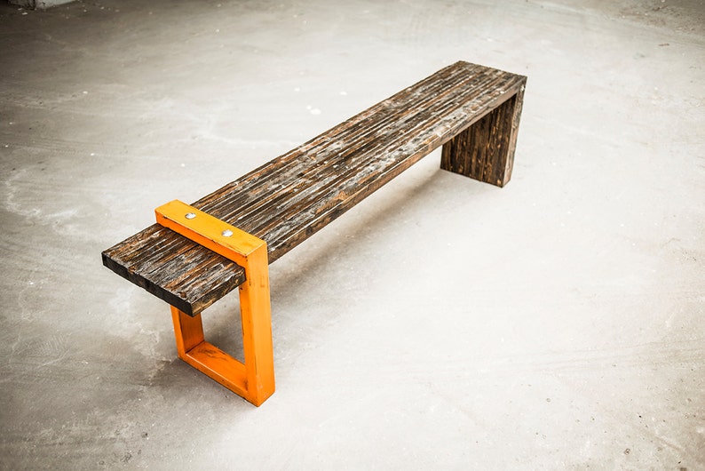 Puede incluir: Un banco de madera con un acabado marr&oacute;n oscuro y patas de metal naranja. El banco tiene un aspecto r&uacute;stico y est&aacute; hecho de madera recuperada.